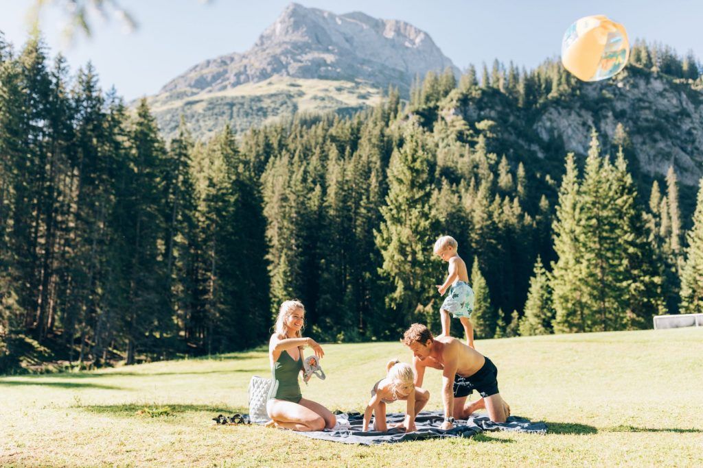 Family of four enjoying the sun in a forested area of Lech with the mountains in the background.