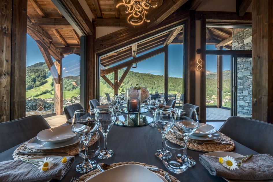 A well-set dining table looking out to views of the Pleney mountain, through large glass windows, as viewed from the interiors of one of the best summer chalets in Morzine, Chalet Griffonner.