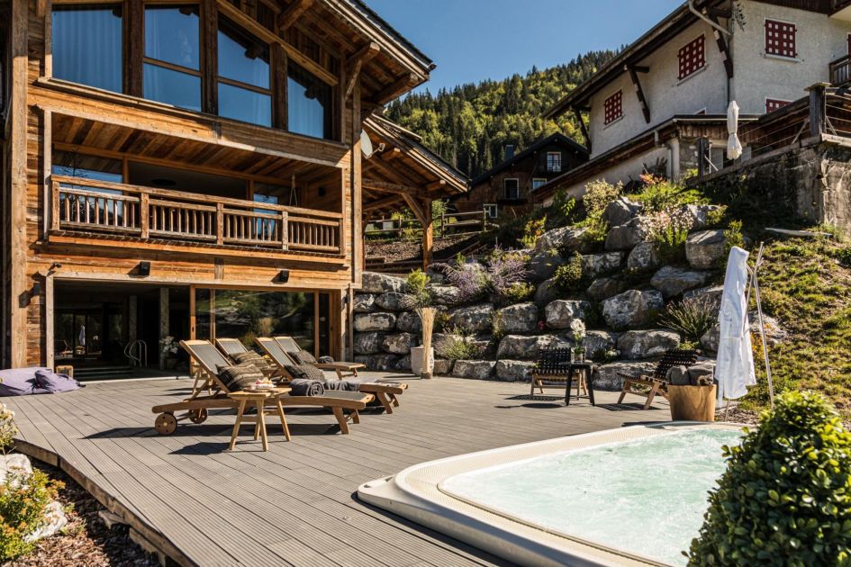 An outdoor hot tub and sun loungers are found on the outdoor decking in front of Chalet Sapphire Gem - one of the best summer chalets in Morzine.