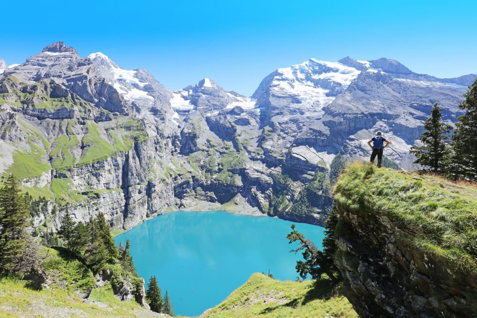 Hiker stood on the crag of the mountain, enjoying the blue waters and views of Lake Oeschinen in Switzerland. Just one of many activities to do on summer holidays to alpine lakes that really let you admire the beauty of the landscape!