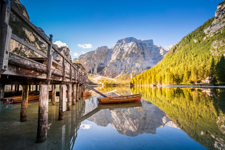 View of Lago di Braies in the Dolomites. Its beautiful mountain scenery is reflected in the waters, where a number of rowing boats lie. Summer holidays to alpine lakes don't come much better than this!