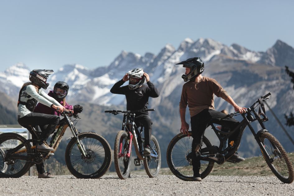 Luxury mountain biking holidays in Morzine are for everyone! Four mountain bikers are deep in discussion here, whilst mountains spread across the background. 