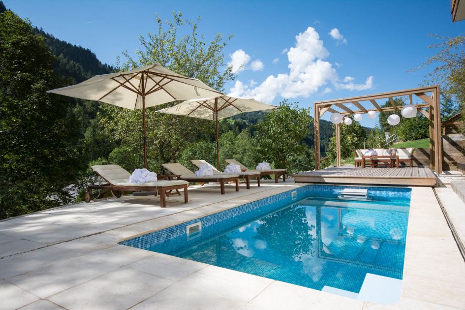 Image of outdoor swimming pool and patio at Chalet Twenty26, with surrounding forest views.