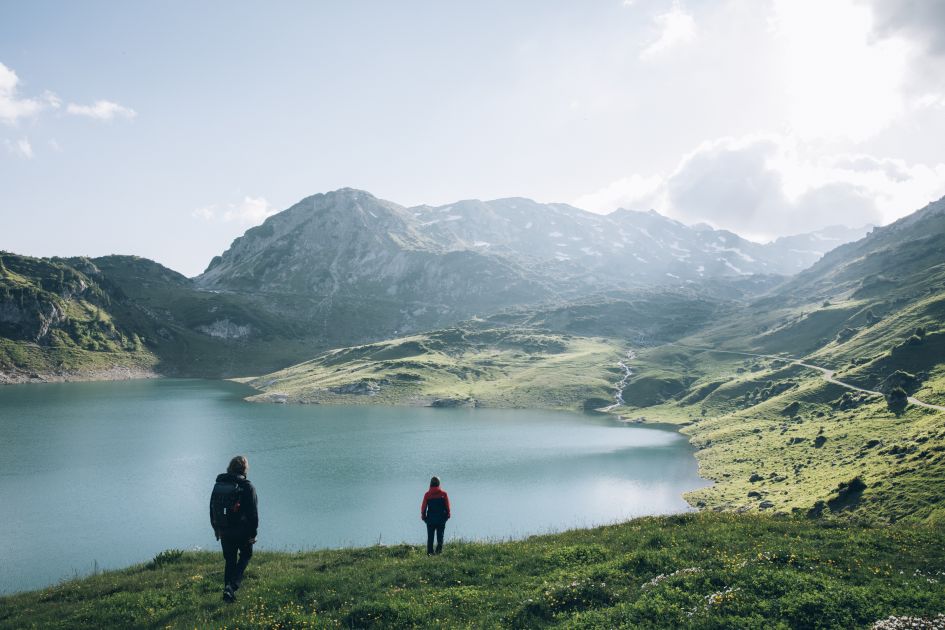 Beautiful alpine landscape of green mountains and a lake, as viewed upon by a pair of hikers on a hike in the Arlberg.