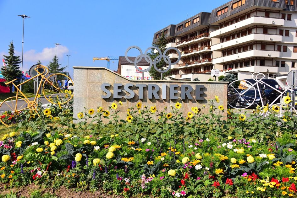 A sign of Sestriere with the Olympic rings above and blooming flowers below.