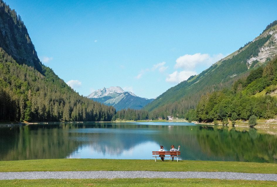 Two people sitting on a bench on the shore of Lac de Montriond, one of the best lakes in the Alps.