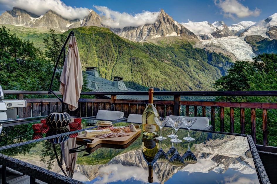 Terrace views from Chalet Hibou in Chamonix, looking out to the Aiguille du Midi and Mont Blanc mountain region with food and drink on the table. A great view to accompany your summer 2025 chalet holiday.