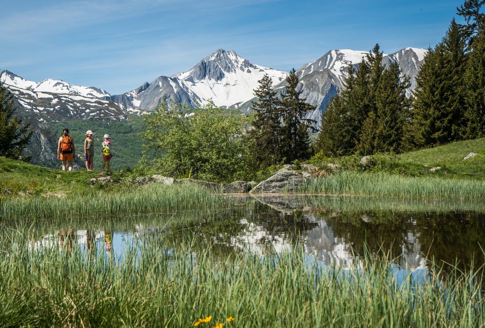 Hiking in the mountains of St Martin de Belleville, a summer activity in for a great lakes and mountains holiday for all to enjoy! Snowy peaks in the distance and a grassy lake in foreground.