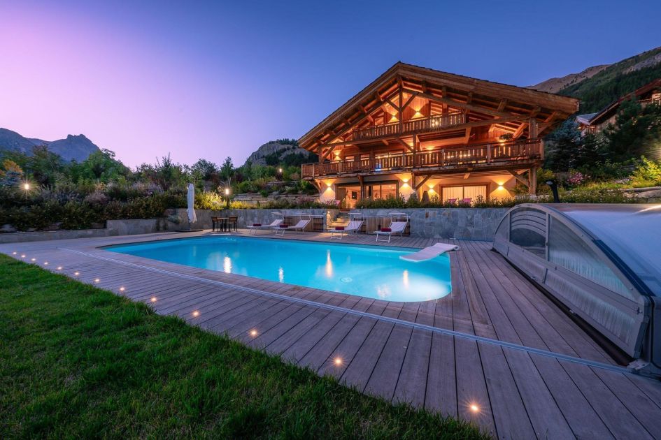 Exterior of Chalet Le Tabuc featuring a pool in the foreground and well-lit chalet - the perfect reason to book a summer alps holiday early for 2025.