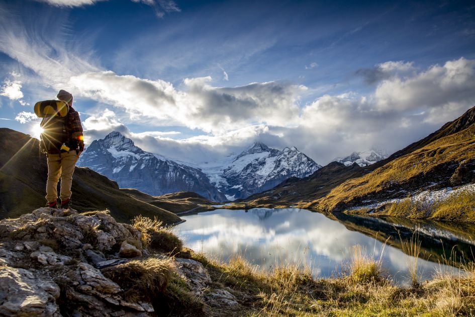 A person overlooking Lake Bachalpsee with the sun shining and mountains in the distance. The type of view you can expect on lakes and mountains holidays in Switzerland.