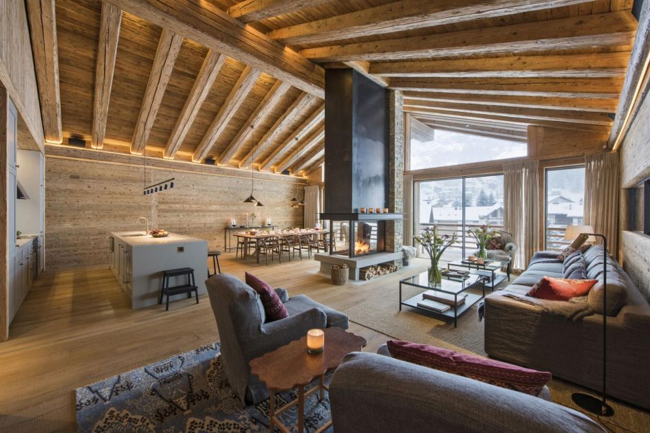 Chalet McKinley's main open-plan living area complete with sofas, central wood-burning fireplace, kitchen and dining table at the back. The chalet lies in a fantastic location for those wanting to explore a variety of lakes and mountains in Switzerland.