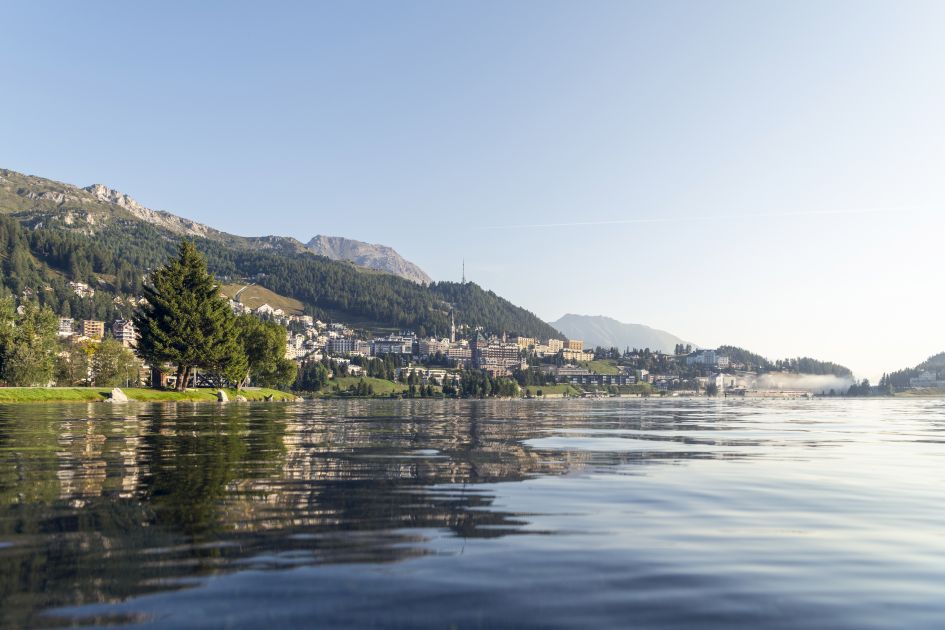 Photo taken from the water's view of Lake St Moritz showing the lake itself and buildings and mountains surrounding the water's edge. St Moritz is the perfect destination to explore lakes and mountains in Switzerland.