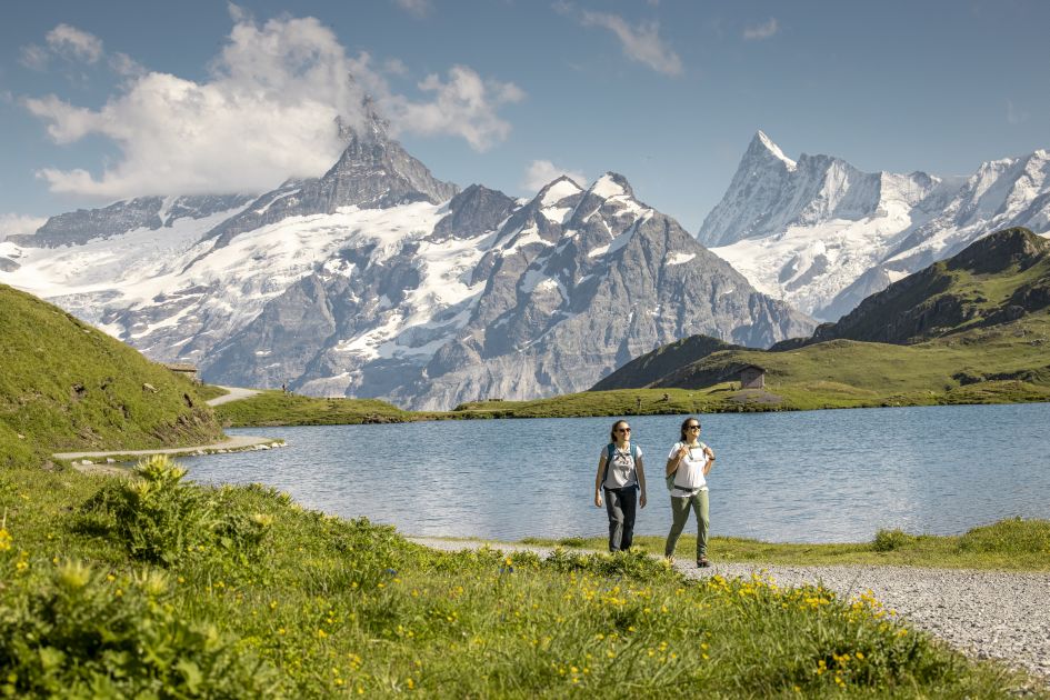 A couple of hikers walking around Lake Bachalpsee in summer. Lying close to Grindelwald, it's one of our recommended destinations when visiting lakes and mountains in Switzerland.