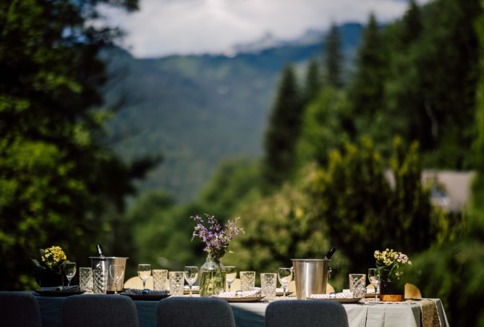 Outdoor dining table adorned with flowers and glasses, in the sunshine. A great place to spend time together on a sustainable mountain holiday