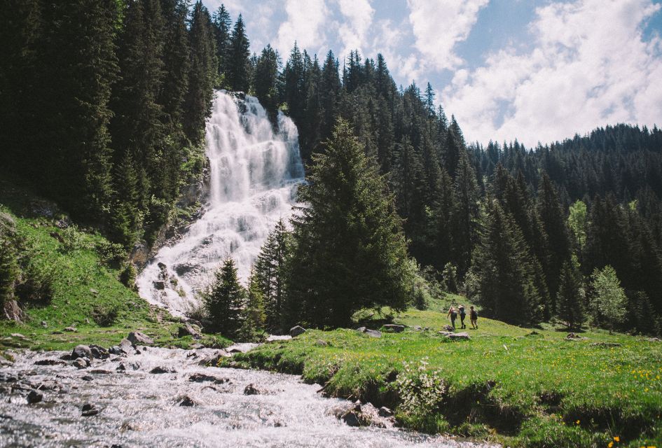 A waterfall in the summer in Morzine, with 3 walkers enjoying the scenery